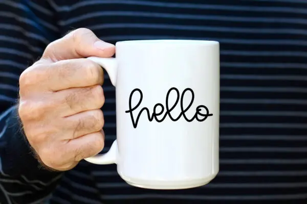 A person holding a coffee mug that says hello.