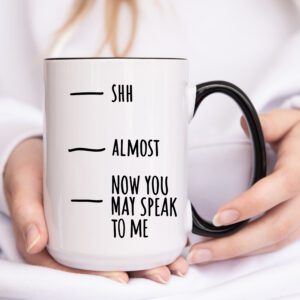 A person holding a coffee mug with the words shh almost and now you may speak to me written on it.