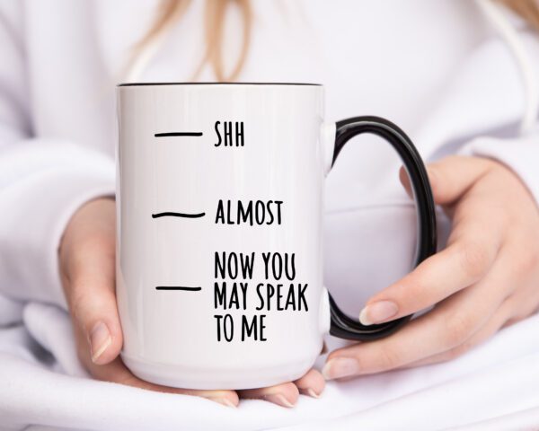 A person holding a coffee mug with the words shh almost and now you may speak to me written on it.