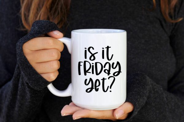 A person holding a coffee mug that says " is it friday yet ?"