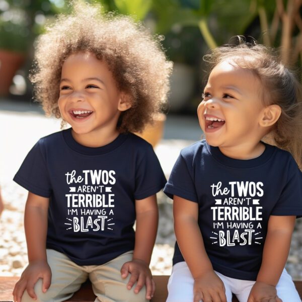 Two children sitting on the ground wearing matching shirts.